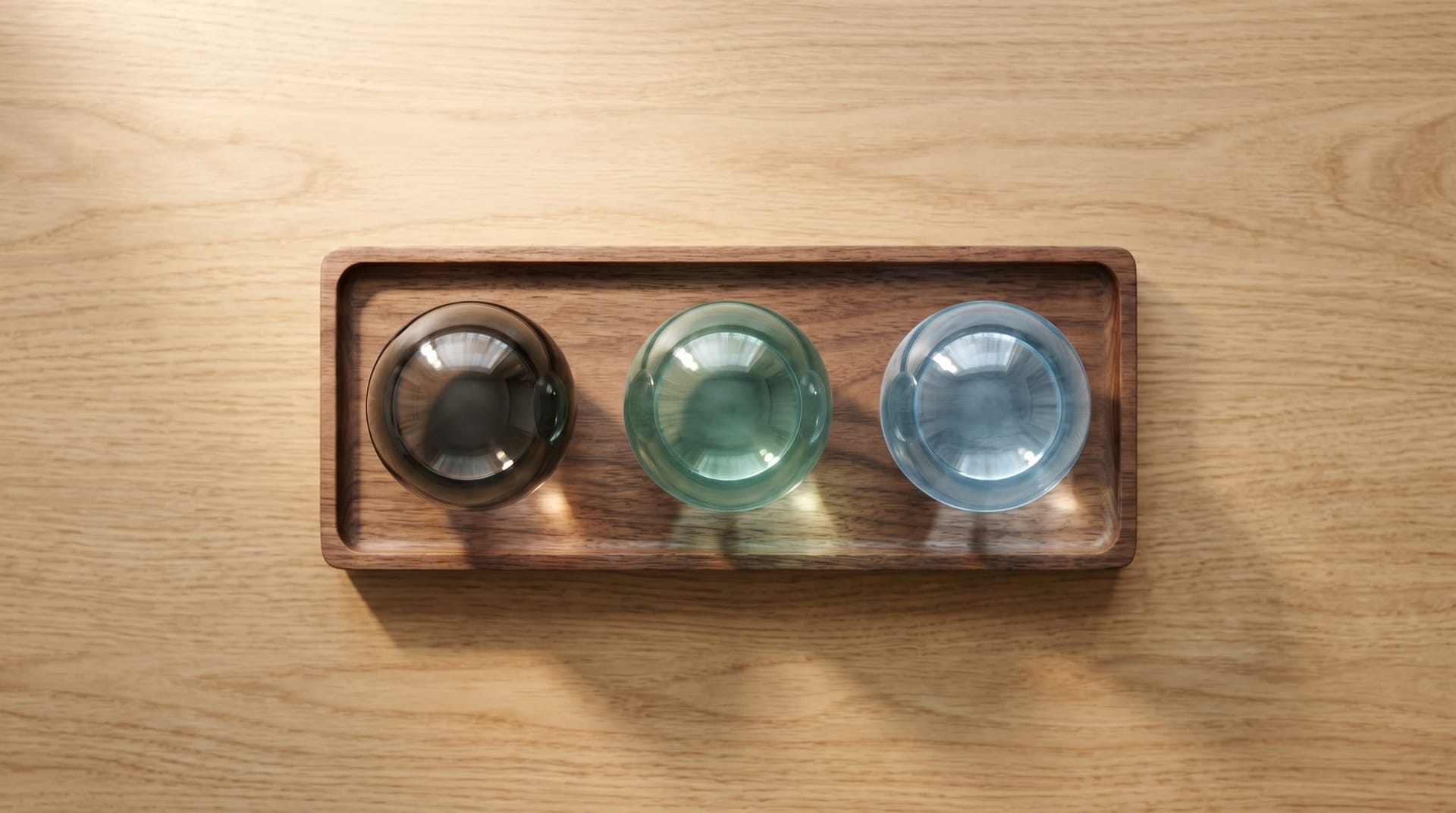 Three differently-tinted but identically-shaped glass orbs on a wooden tray on a clean desk, representing substitutable AI model layers — today's LLM, a world-model-enabled successor, and a future variant.